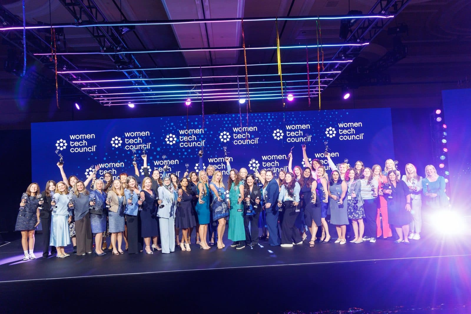 The 2026 Women Tech Awards honorees together on stage at The Grand America Hotel, holding their trophies up.